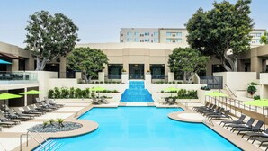 A swimming pool with a central staircase, surrounded by lounge chairs and umbrellas, with a building in the background. - Element by Marriott San Diego Mission Valley (San Diego)