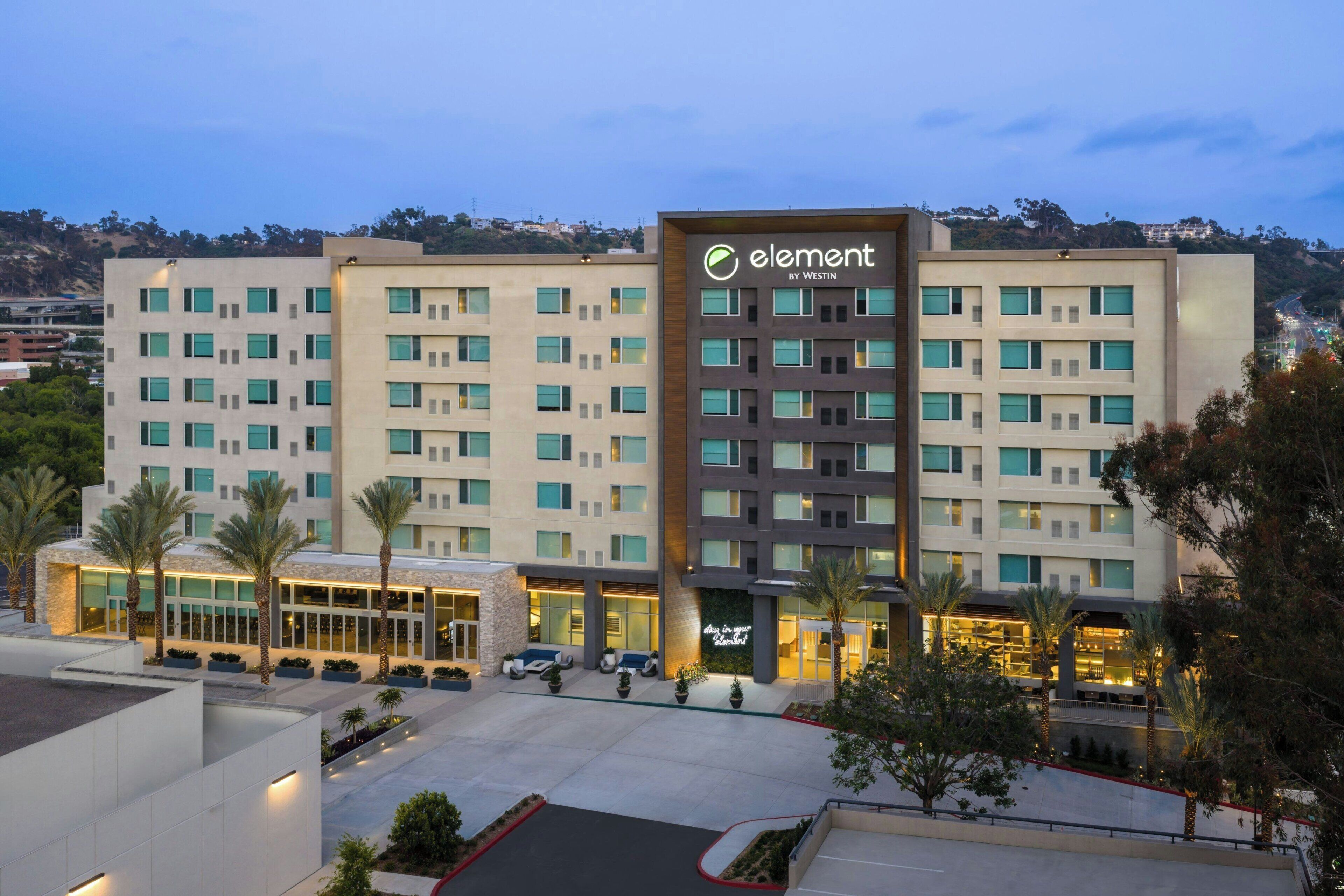 Un hotel con una torre central que muestra el logo 'element by Westin', varios pisos con patrones de ventanas uniformes y un patio ajardinado con palmeras.