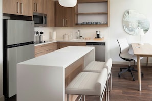 Una cocina moderna con una isla central, electrodomésticos de acero inoxidable y una zona de comedor con una silla y una mesa.