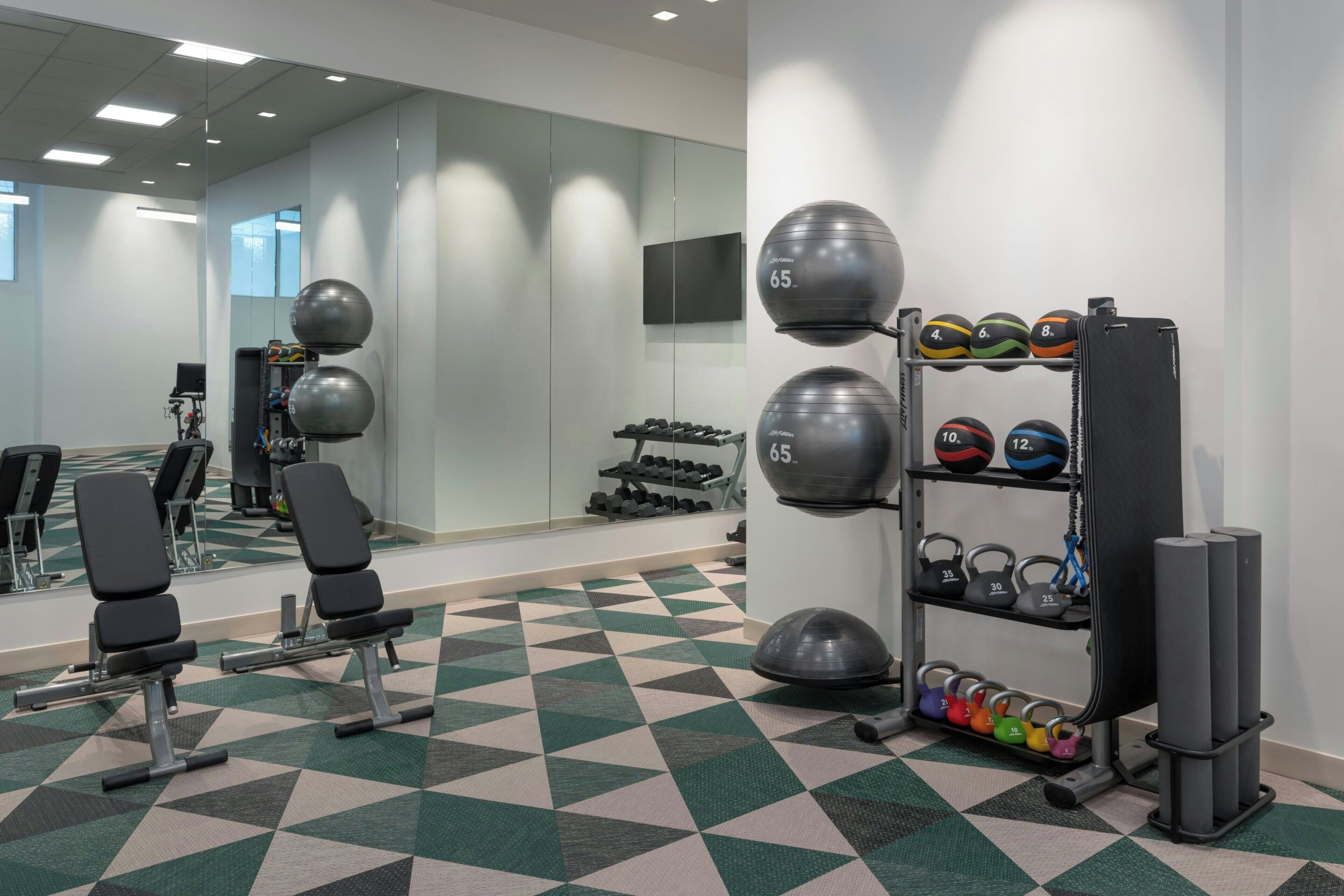 Uma academia com equipamentos de ginástica, incluindo um banco, halteres e uma estrutura com bolas de medicine.