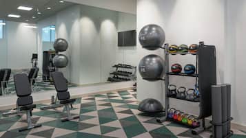 Uma academia com equipamentos de ginástica, incluindo um banco, halteres e uma estrutura com bolas de medicine.
