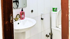 Ein Badezimmer mit weißen Fliesen, einem Waschbecken, einem Spiegel, einer Dusche und einer Toilette.