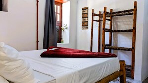 Ein Zimmer mit einem Bett, einem Holzbett und Vorhängen am Fenster sowie einem Wandbild.