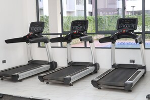 Three stationary treadmills in a room with large windows, a tiled floor, and a white wall. - Welcome to your modern, peaceful escape just minutes from the airport &CBD (Nairobi)