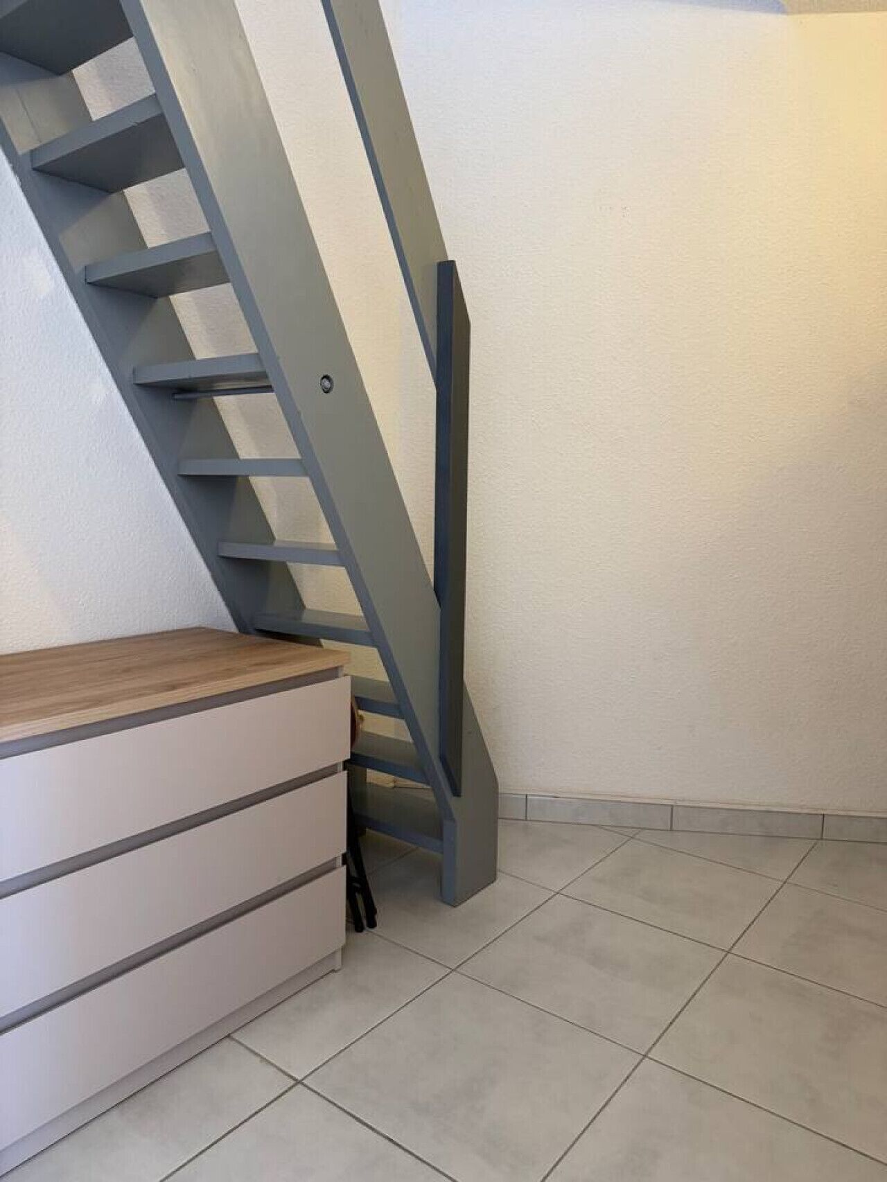Een trap met een houten leuning en een grijze metalen zijkant, die naar een lager gelegen niveau leidt.