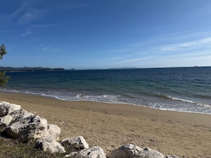 Ein Strand mit blauem Himmel, ruhiger See und felsigem Vordergrund.