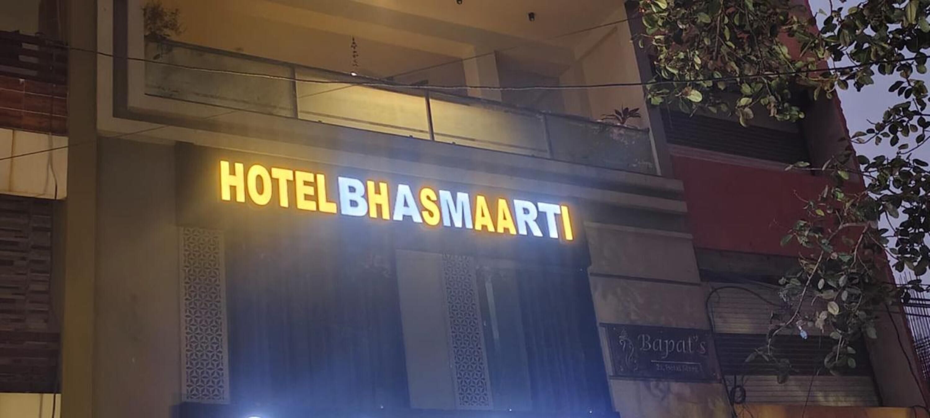 A hotel sign with the name 'HOTEL BHASMAARTI' illuminated.