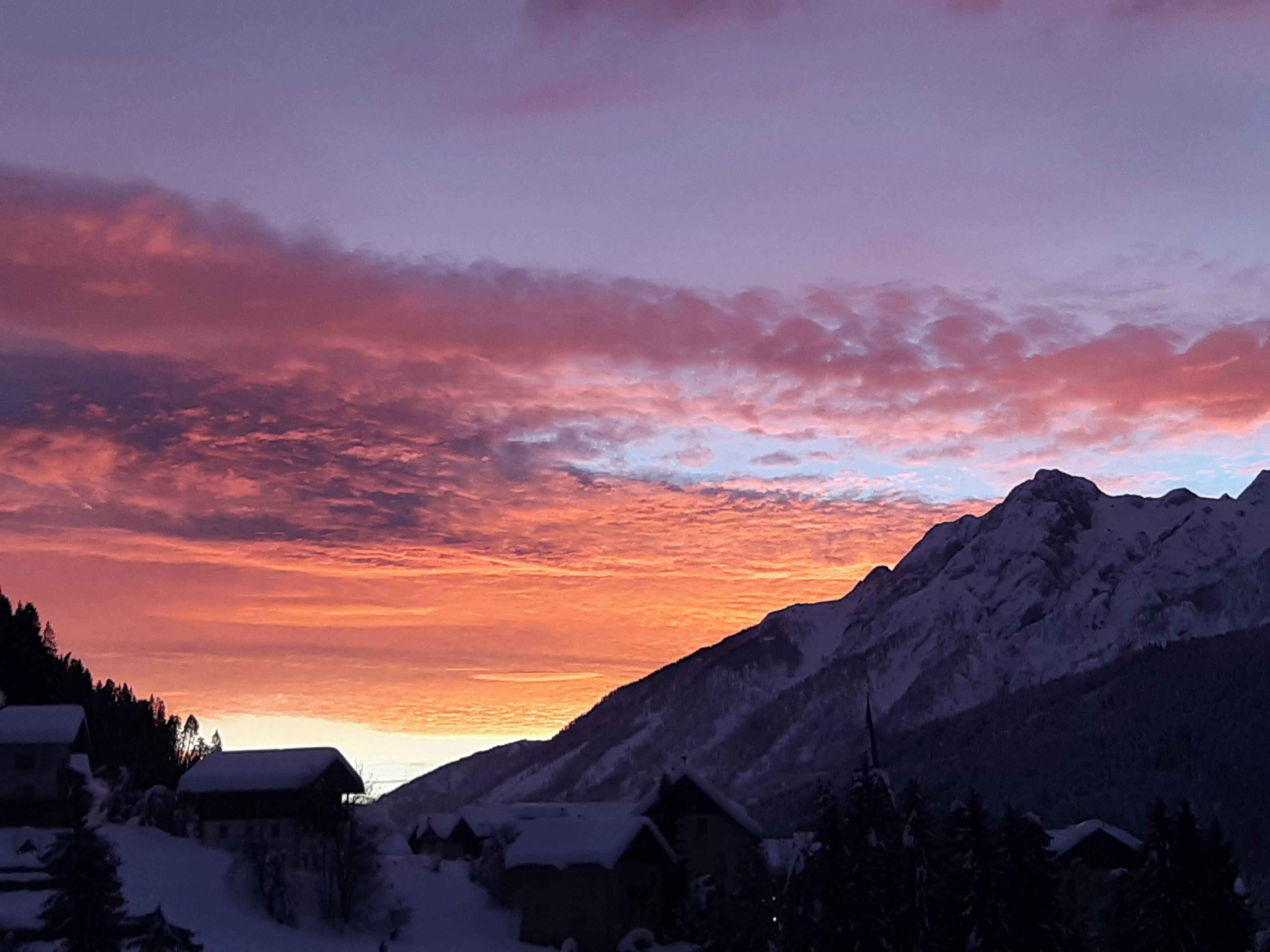 A mountainous landscape with snow-covered houses and a sunset sky.