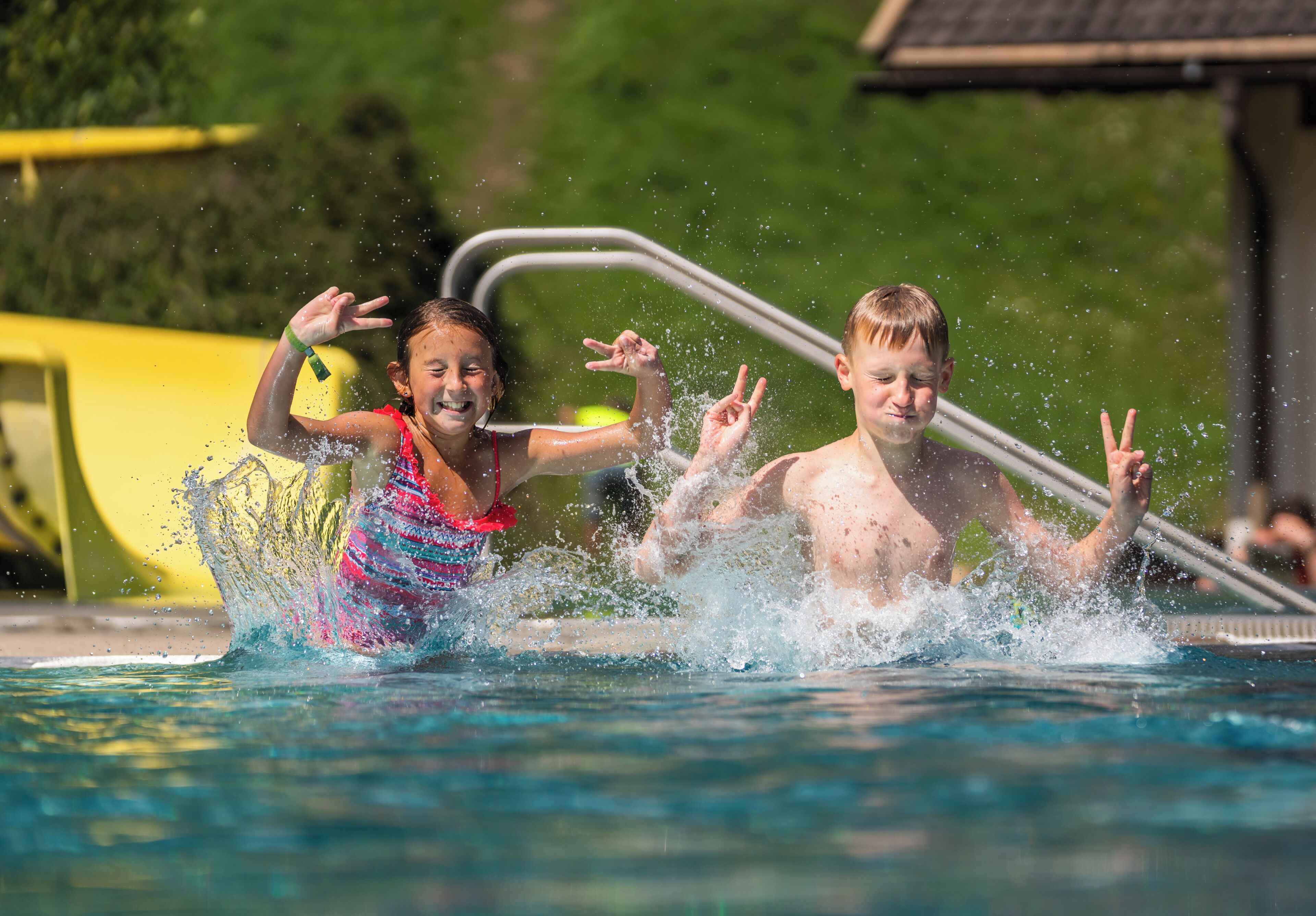 Two children splashing in a pool with a metal ladder in the background.