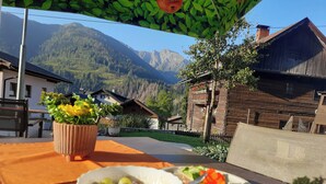 Una mesa con un tazón de ensalada de frutas y un plato con un sándwich, una planta en maceta y vistas de un paisaje montañoso.
