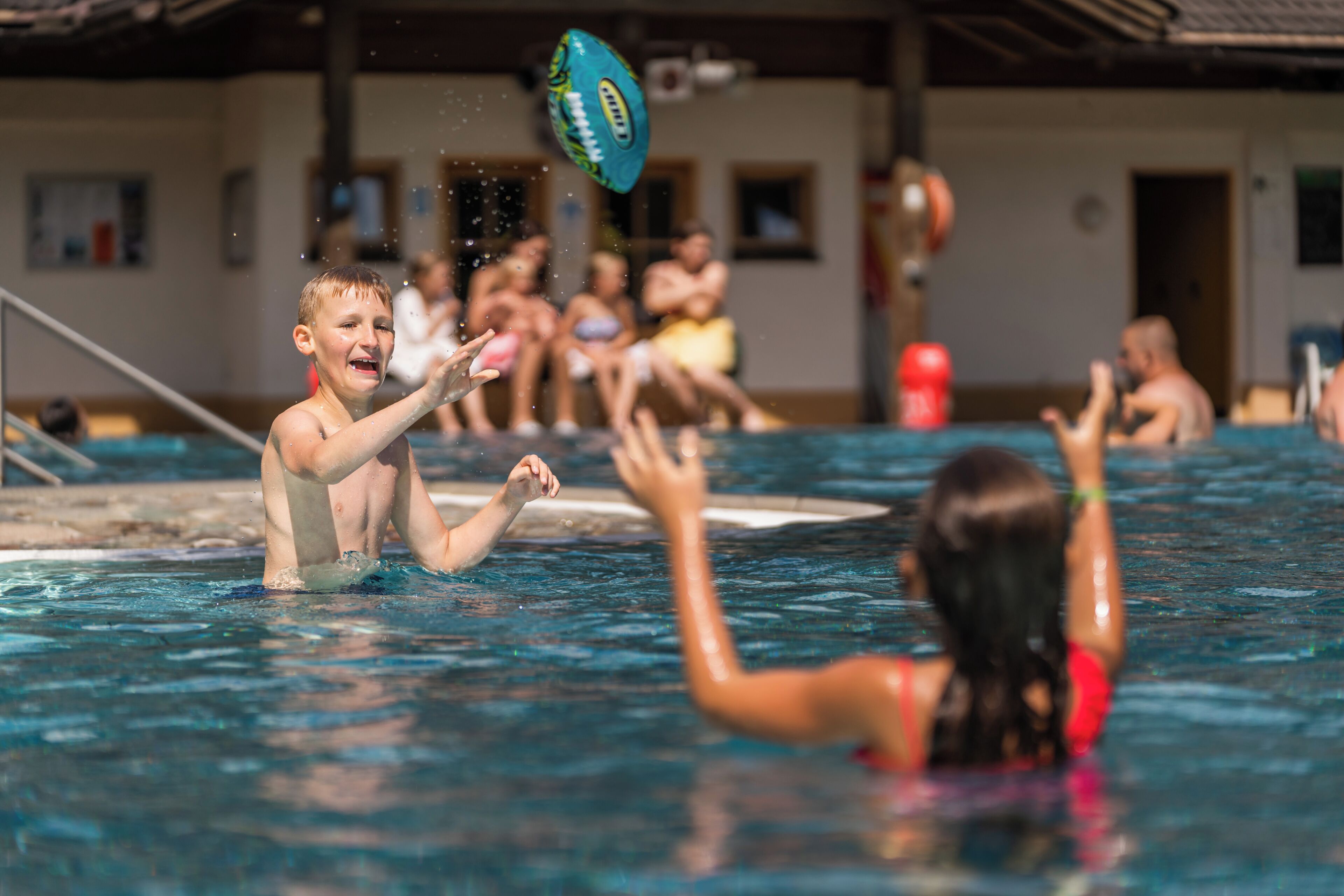 Una piscina con gente jugando, un trampolín y un tobogán de agua.