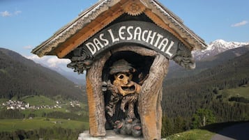 Une structure en bois portant l’inscription « DAS LESACHTAL » et ornée d’une sculpture, le tout se dressant sur un fond de paysage montagneux.