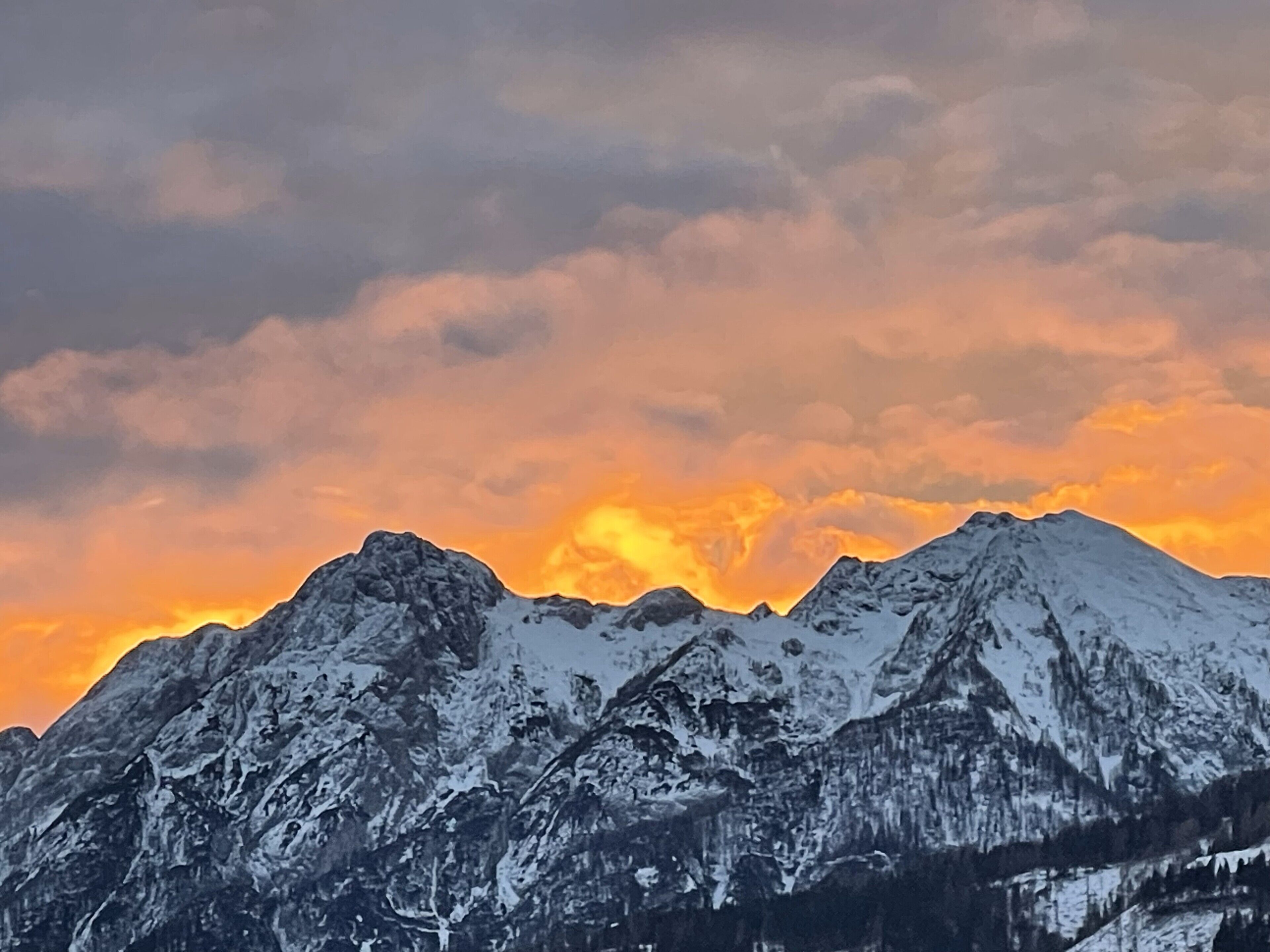 A mountain range with snow-covered peaks and a sunset sky.