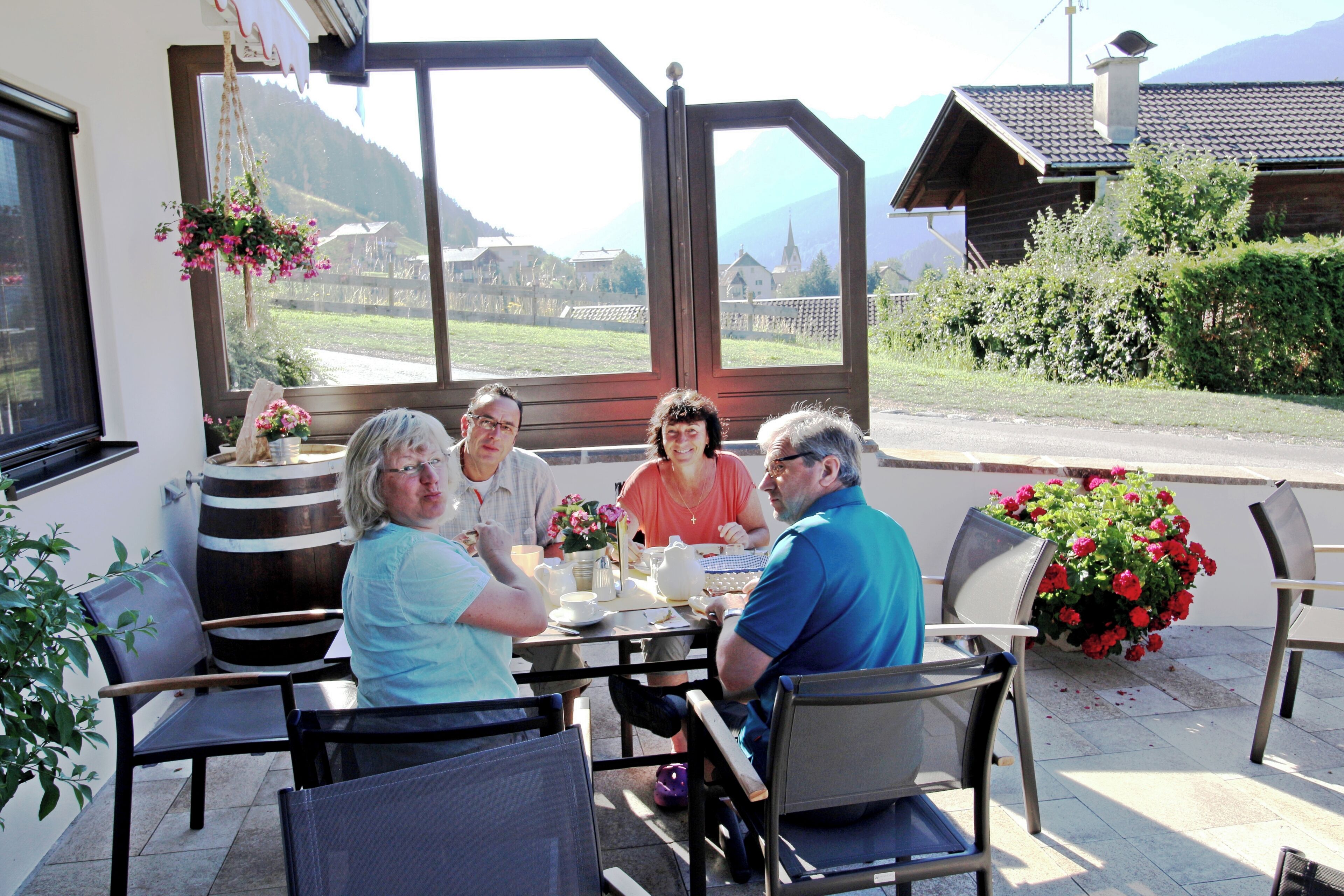 Un grupo de personas cenando en una mesa al aire libre con vistas a un paisaje montañoso.