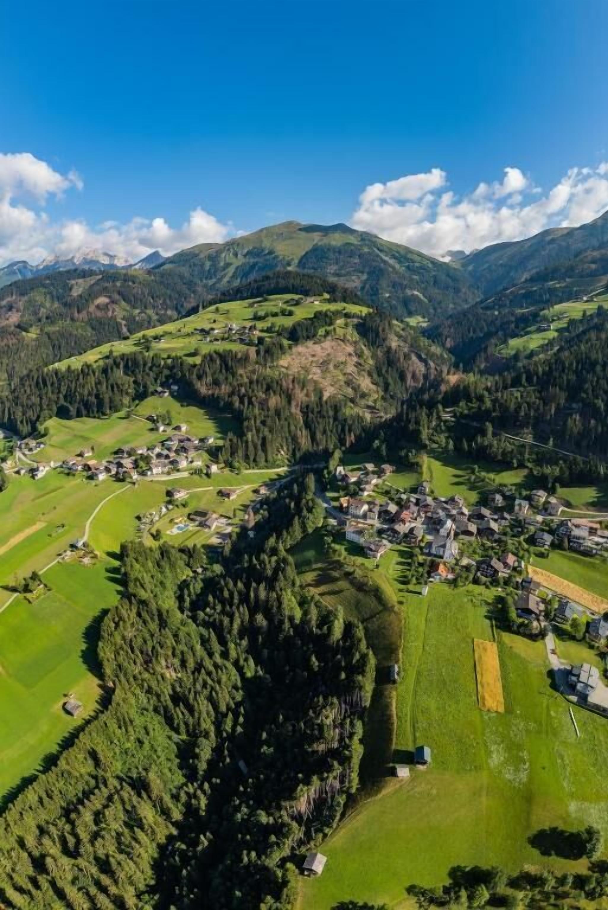 Ein Dorf mit Häusern, grünen Feldern und Bergen im Hintergrund.