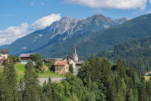A mountain village with a church, houses, and dense forest. - Das kleine Berghotel (Lesachtal)
