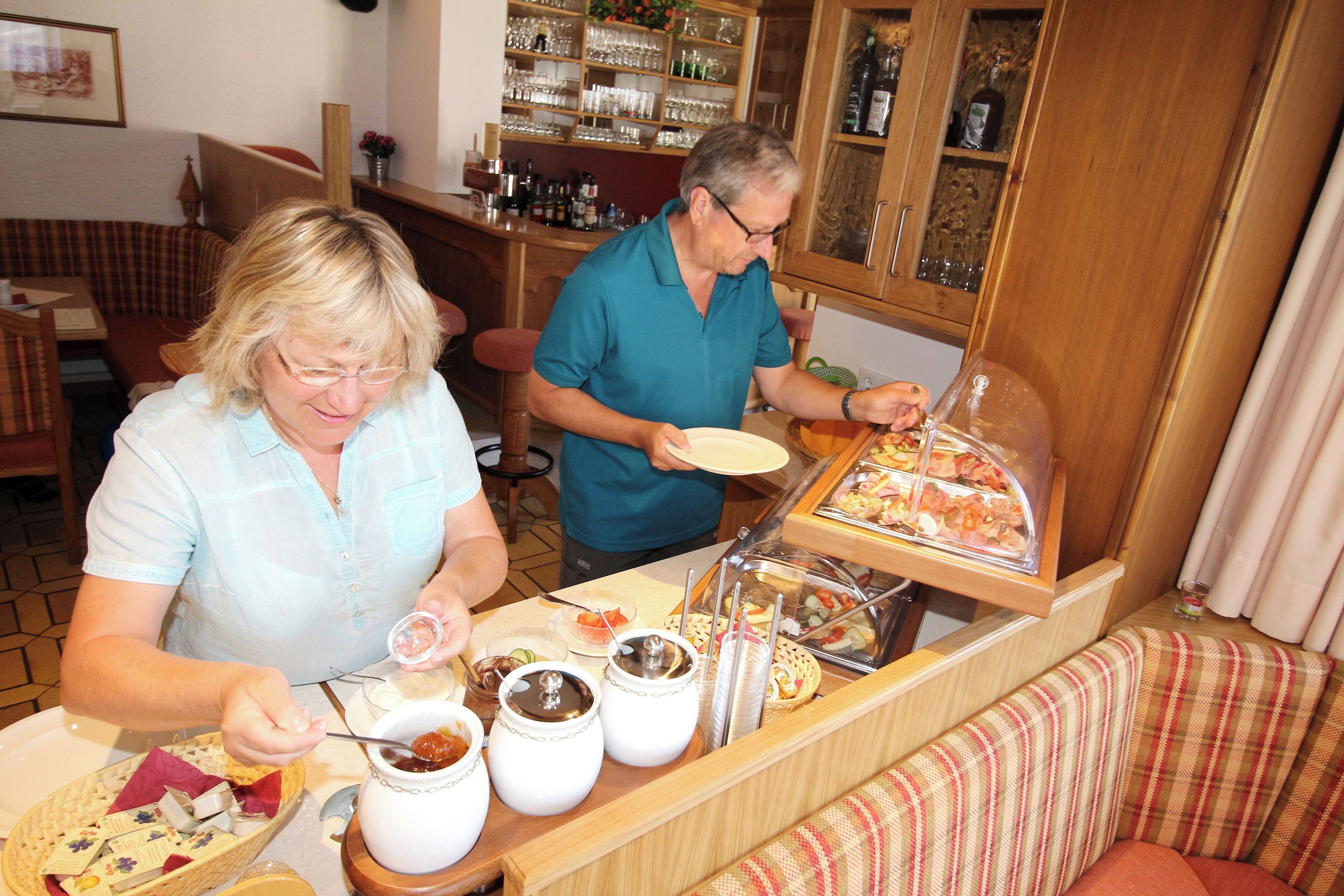 Un buffet est installé dans une pièce meublée en bois, avec des plats et une station de boissons, et un bar est visible à l’arrière-plan.