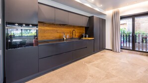 A modern kitchen with dark cabinetry, a wooden backsplash, and a large window with a view of greenery. - Santopaolo Boutique Apartment  (Naples)