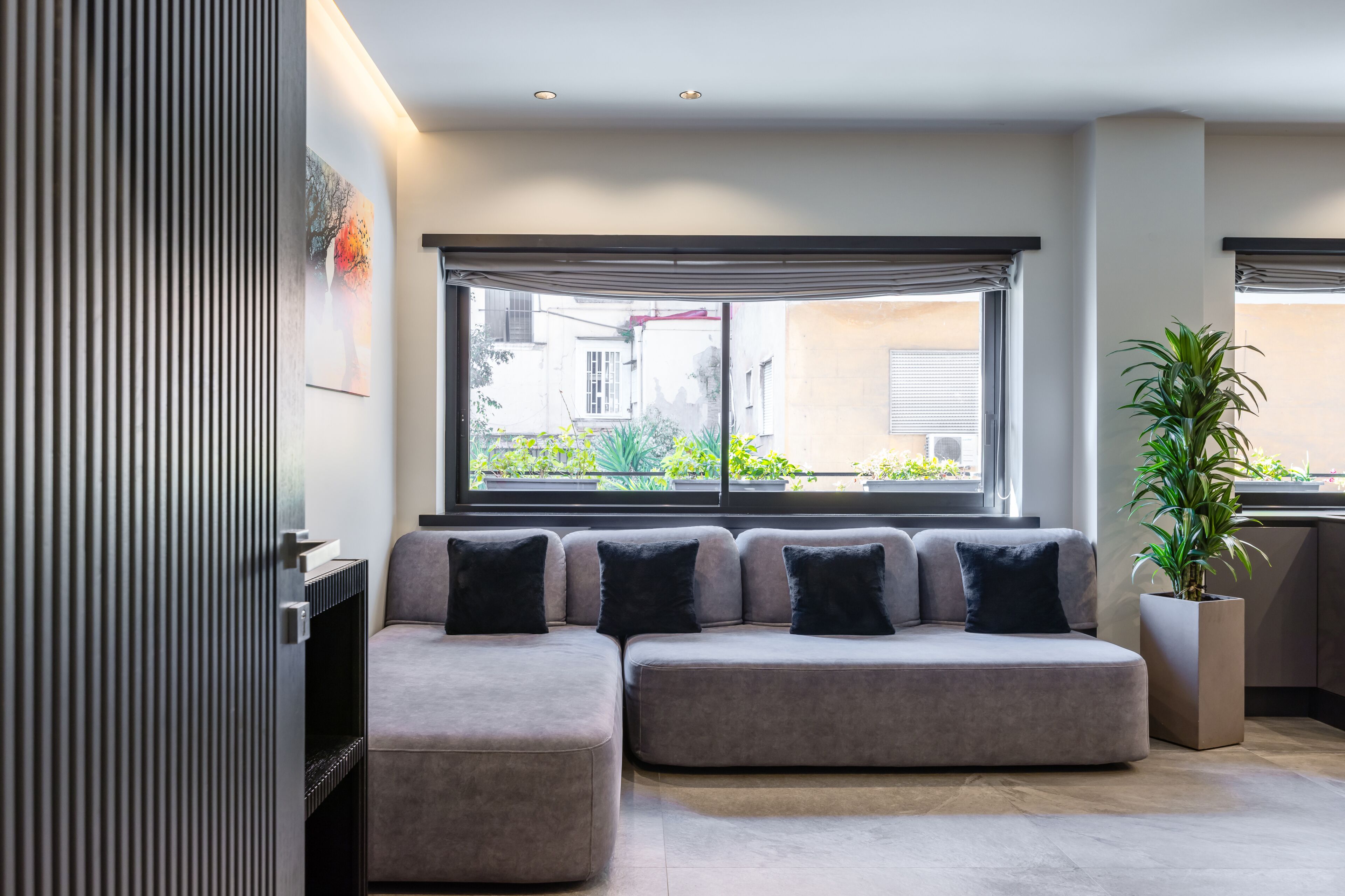 A modern living room with a sectional sofa, a potted plant, and a large window with blinds.