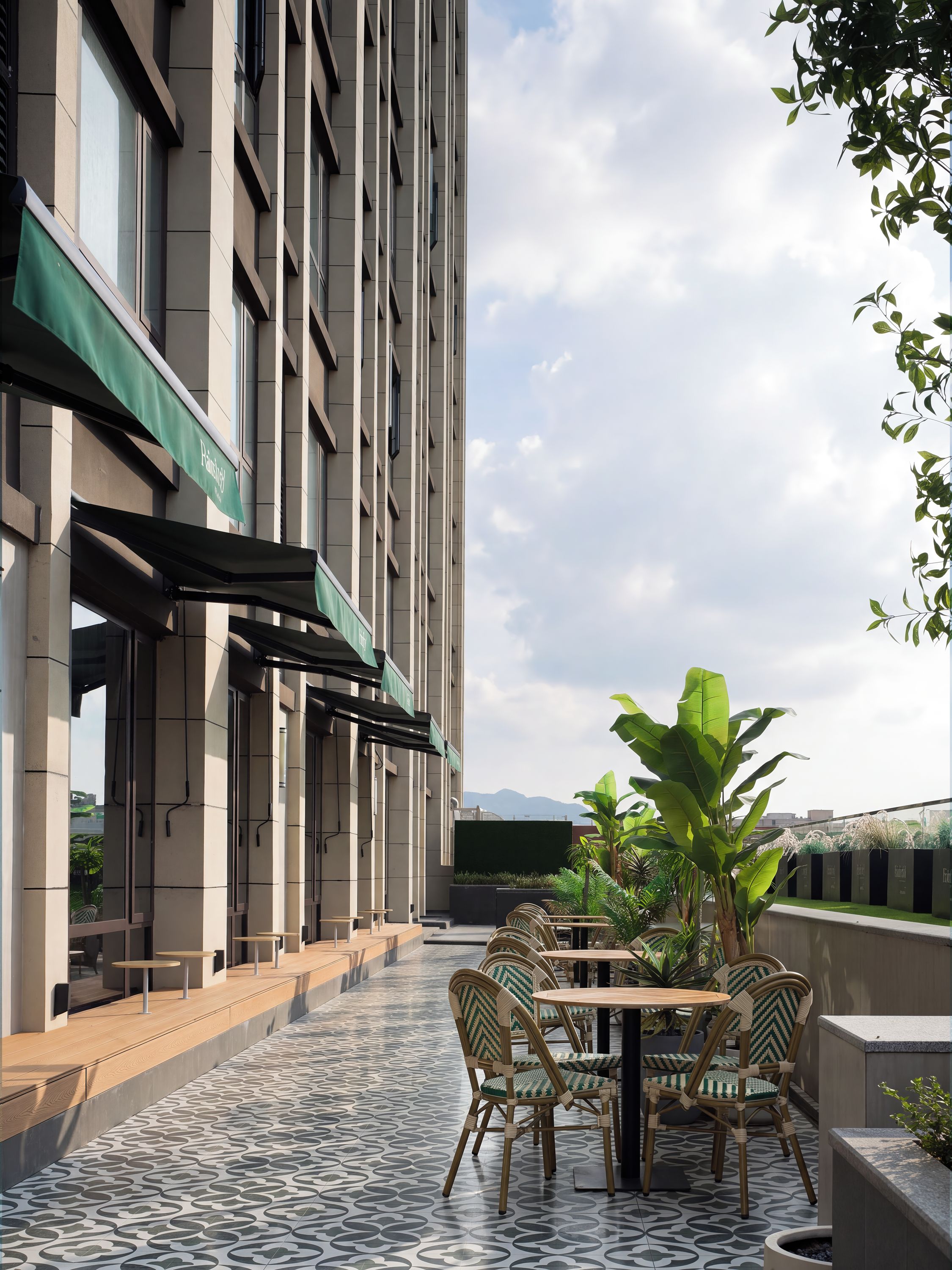 A modern outdoor seating area with a patterned floor, wicker chairs, and a view of a tall building.