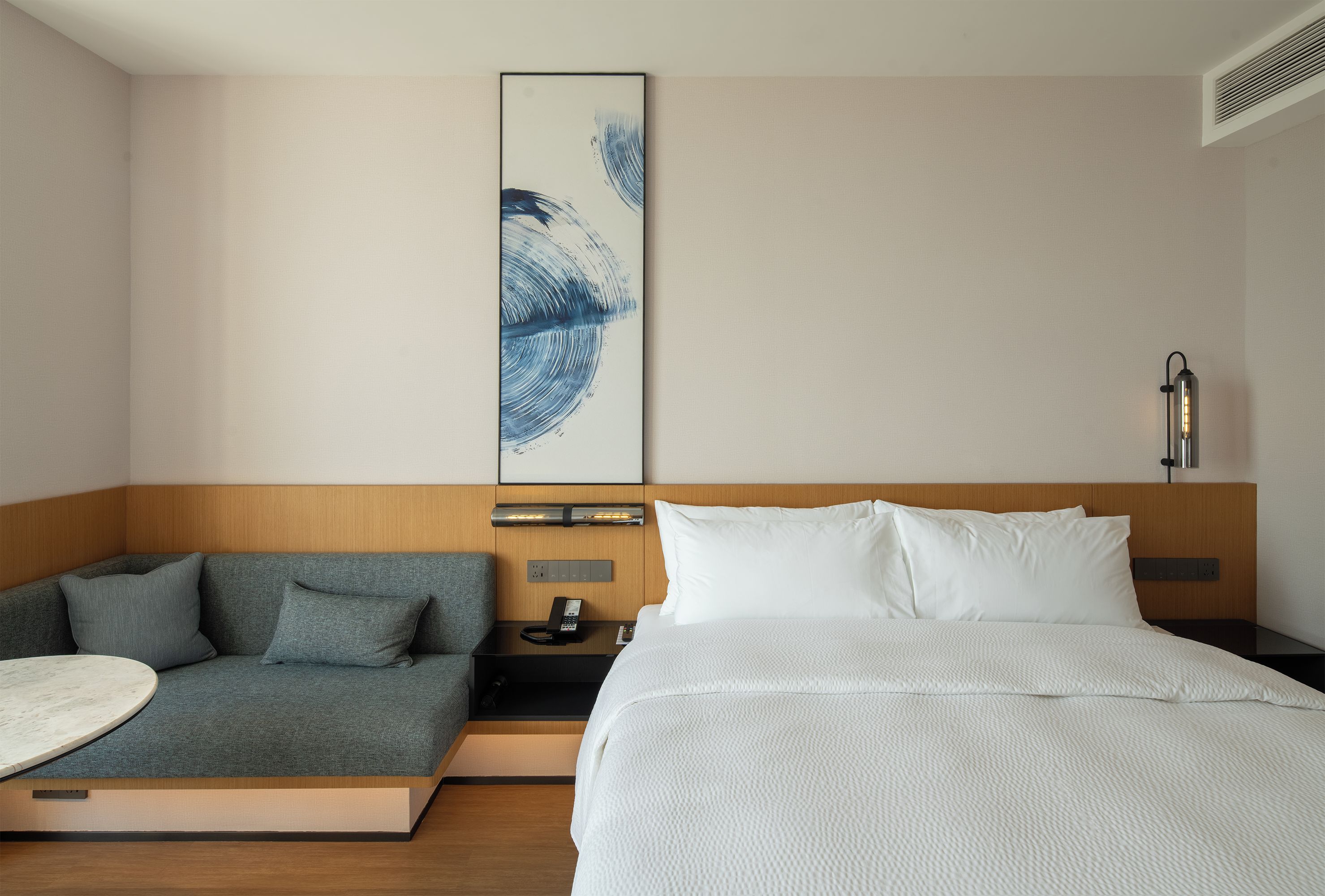 Una habitación de hotel con cama, sofá, mesita de noche con lámpara y una obra de arte en la pared.