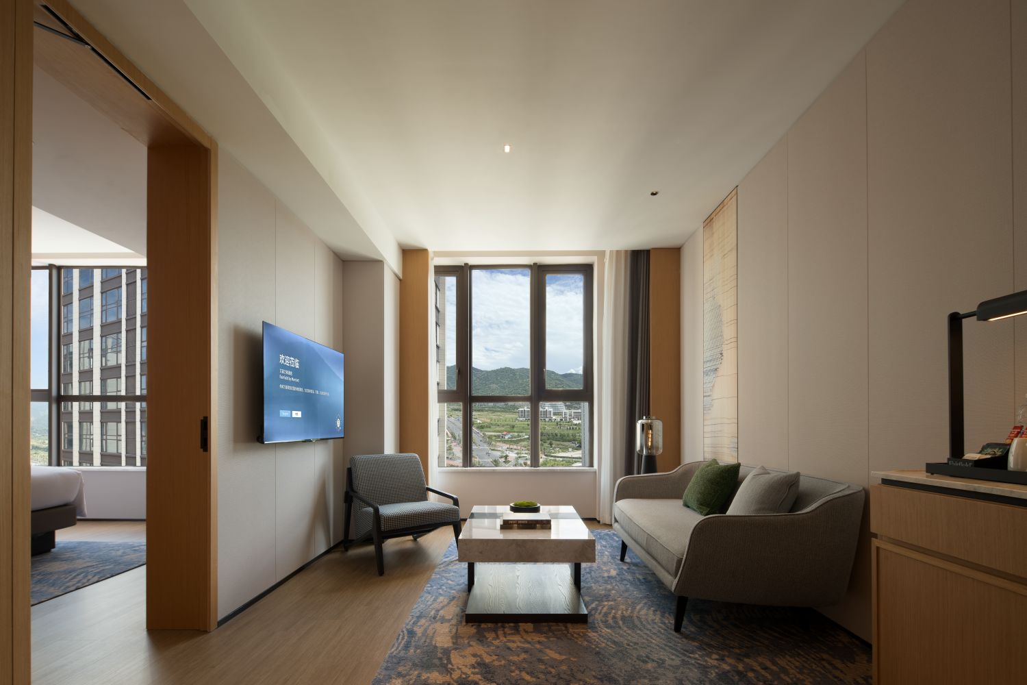 Una sala de estar moderna con un ventanal grande, un televisor de pantalla plana, un sofá, un sillón y una mesa de centro.