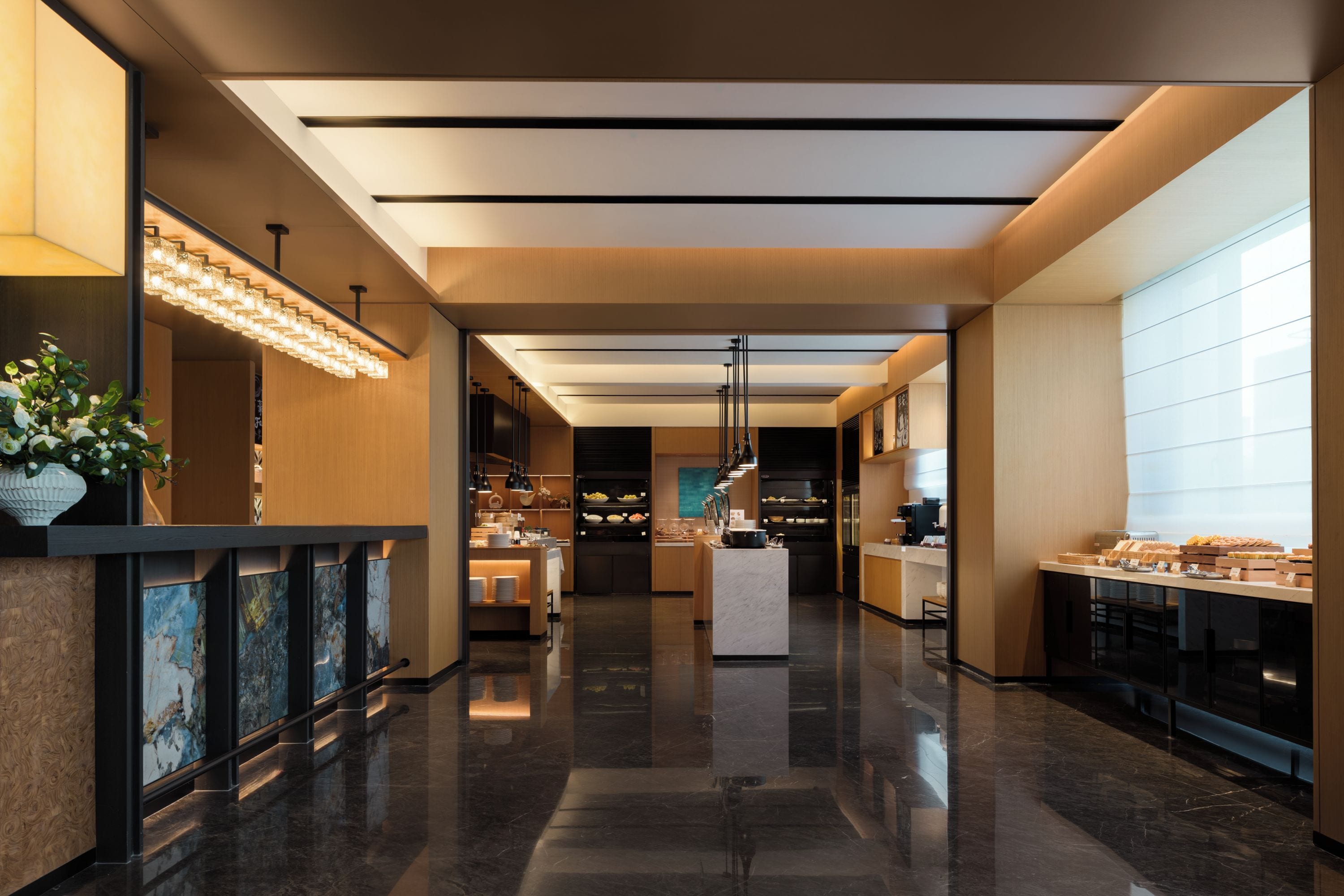 A modern hotel lobby with a central reception desk, a glass partition, and a buffet area.