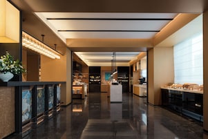 A modern hotel lobby with a central reception desk, a glass partition, and a buffet area.