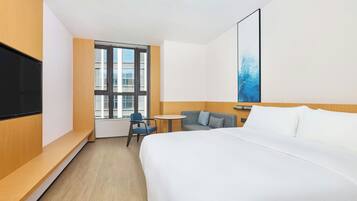 Ein Hotelzimmer mit Bett, Fernseher, kleinem Tisch, Stuhl und Fenster mit Blick auf Gebäude.