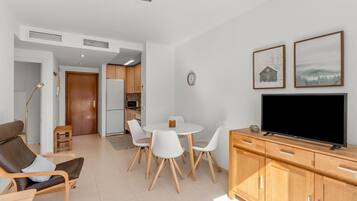 Ett modernt vardagsrum med en soffa, ett matbord med stolar, en tv placerad på ett träskåp och ett kök i bakgrunden.
