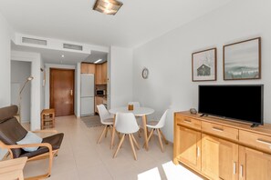 Ein modernes Wohnzimmer mit einer Couch, einem Esstisch mit Stühlen, einem Fernseher auf einer Holzkommode und einer Küche im Hintergrund.