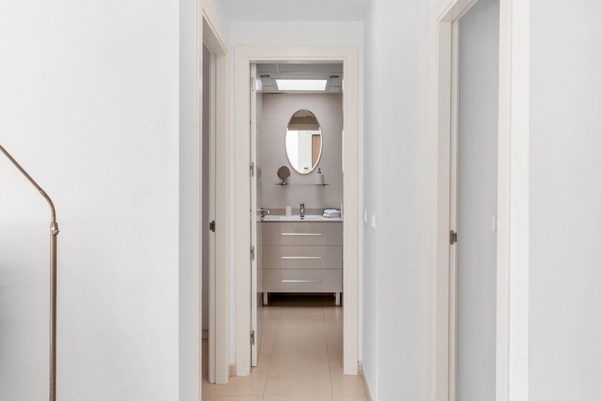Un pasillo que conduce a un baño con espejo, lavamanos y cajones para guardar objetos.