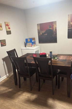 A dining area with a wooden table and chairs, a small white cabinet, and a framed picture on the wall.