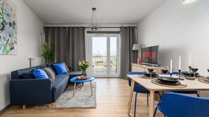 Ein modernes Wohnzimmer mit einer Couch, einem Couchtisch, einem Esstisch und einem Fernseher, der 'NETFLIX' anzeigt.