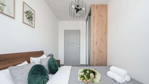 Ein ordentlich bezogenes Bett mit Kissen, einem Blumenstrauß und gerollten Handtüchern, ausgestattet mit einer grauen Tagesdecke.