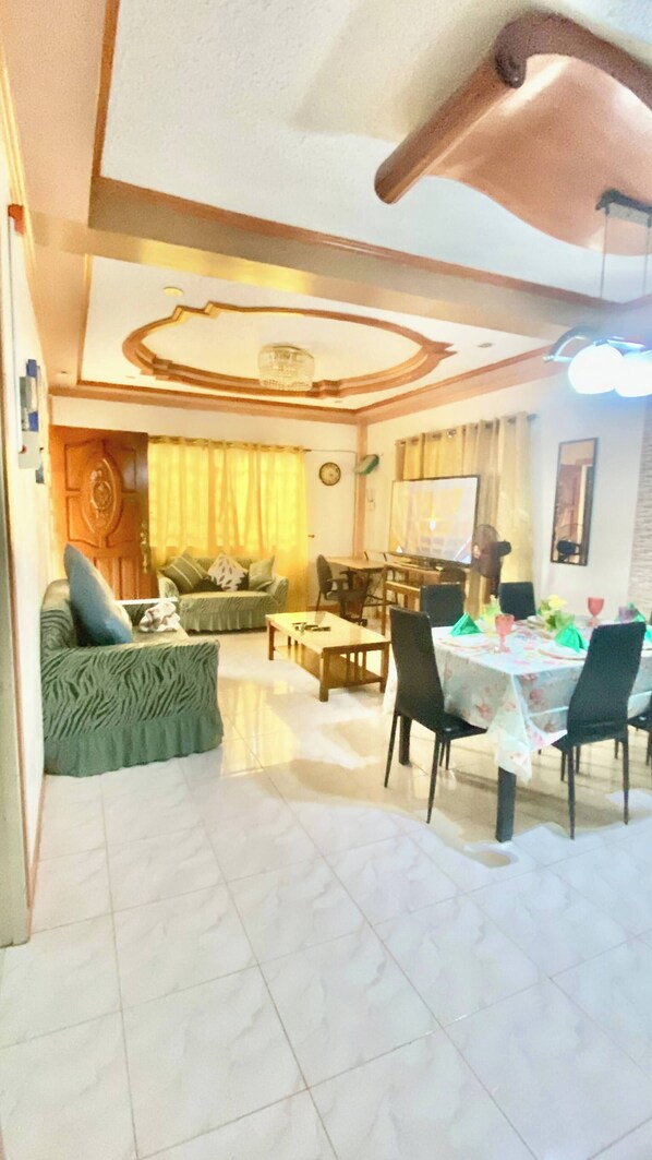 A living room with a sofa, a dining table set for four, and a kitchen area in the background.