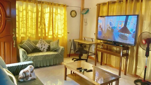 Una sala de estar con sofá, televisión, mesa de centro y cortinas.