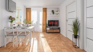 A modern living room with a dining area, a TV displaying 'NETFLIX,' and a potted plant. - Lumina apart with balcony in heart Warsaw (Warszawa BIG)