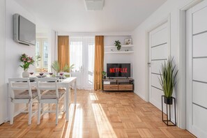 Ein modernes Wohnzimmer mit Essbereich, einem Fernseher, der 'NETFLIX' zeigt, und einer Topfpflanze.