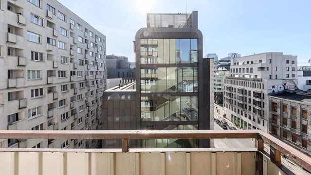 A high-rise building with multiple balconies, a glass facade, and a view of the street below. - Lumina apart with balcony in heart Warsaw (Warszawa BIG)