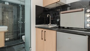 A modern kitchen with a built-in oven, a coffee maker, and a glass shower enclosure. - Tower 15 | Deluxe Studio 402 (Thessaloniki)