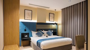 A modern hotel room with a large bed, a bedside table, a chair, and a headboard with built-in lighting. - Lamar Park Hotel Al Olaya (Tabuk)