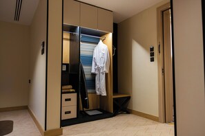 A walk-in closet with a hanging robe, a vacuum cleaner, and a small bench. - Lamar Park Hotel Al Olaya (Tabuk)