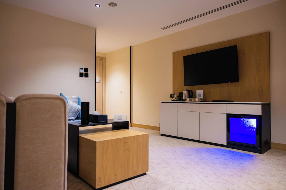 Een moderne hotelkamer met een bank, een houten bijzettafeltje, een flatscreen televisie aan de muur en een inbouwhaard met blauw licht.