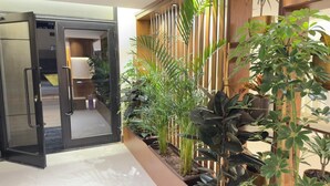 A modern hotel lobby with a glass door entrance, a wooden reception desk, and a variety of indoor plants. - Lamar Park Hotel Al Olaya (Tabuk)