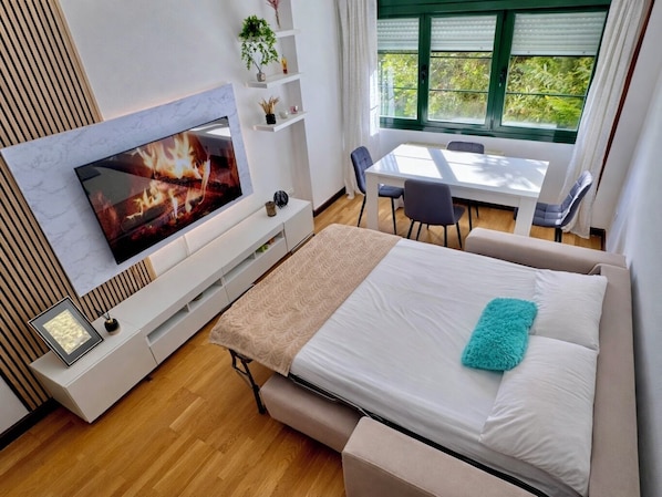 Una habitación de hotel moderna con cama, televisor, mesa de comedor y sillas.