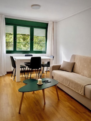 Una habitación con una mesa de comedor, sillas, un sofá, una mesita con una vela y una ventana con persianas.