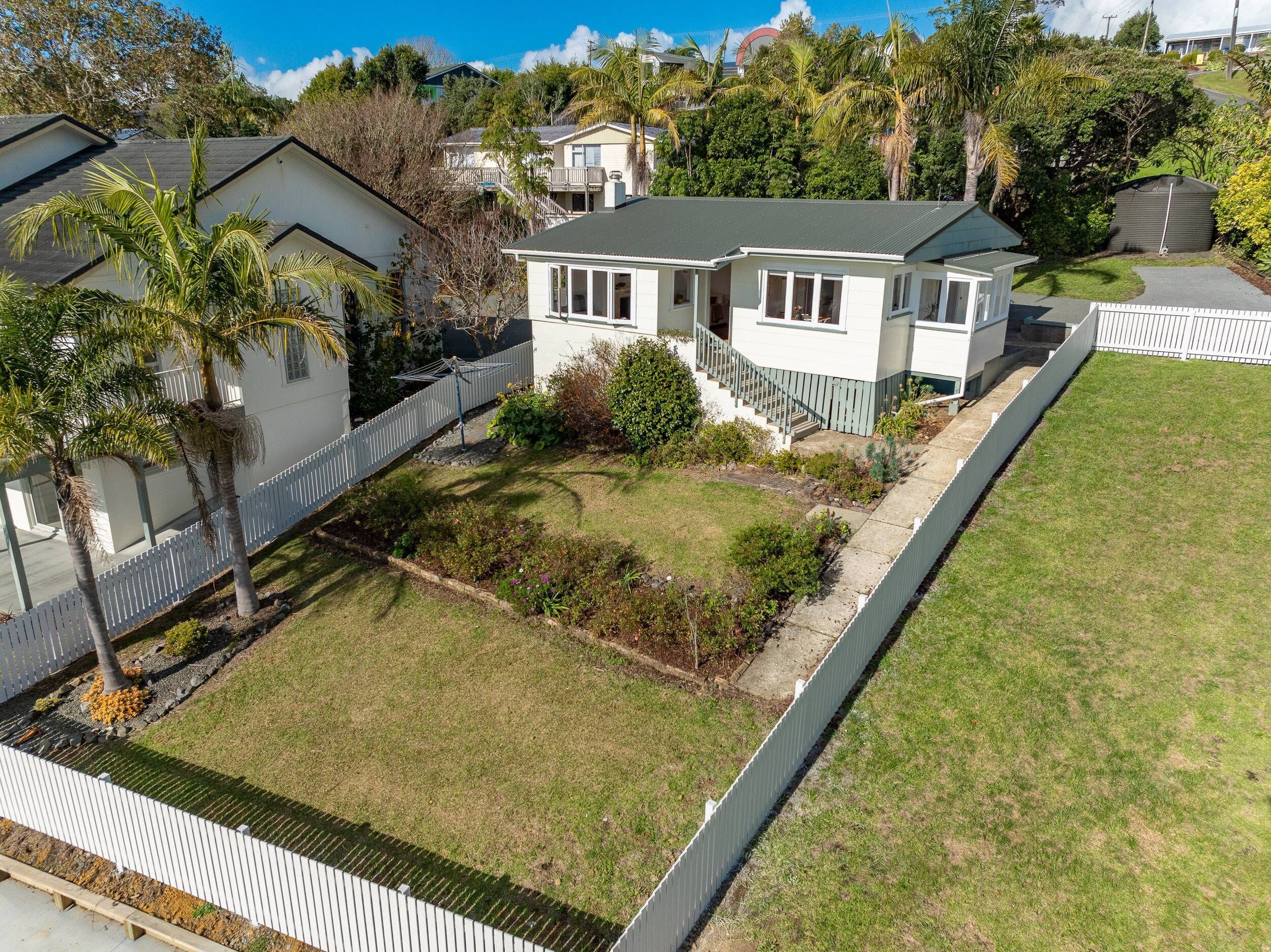 A residential house with a front yard, a white picket fence, and a small garden area.