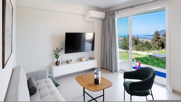 Ein modernes Wohnzimmer mit Flachbildfernseher, einer Couch, einem Couchtisch und einem Sessel.