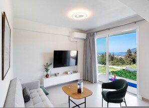 A modern living room with a flat-screen TV, a sofa, a coffee table, and a chair. - Asmira Apartments (Lefkada)